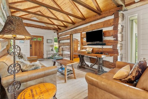 Cozy cabin interior with wooden beams, leather sofas, a coffee table, and a TV mounted on a rustic wall.