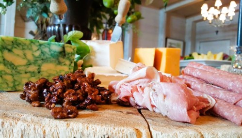 A wooden board featuring various cheeses, cured meats, and nuts, set in a cozy dining environment.