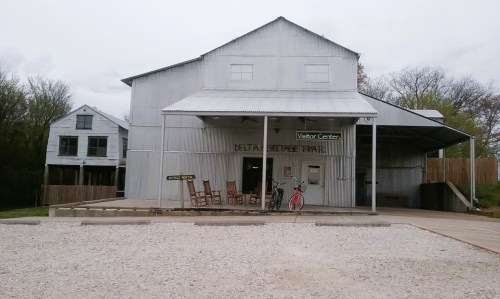 A rustic visitor center with a metal exterior, rocking chairs on the porch, and a bike parked outside.