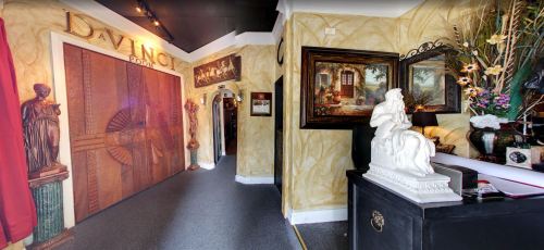 Interior of a gallery featuring ornate walls, artwork, and a statue, with a large wooden door in the background.