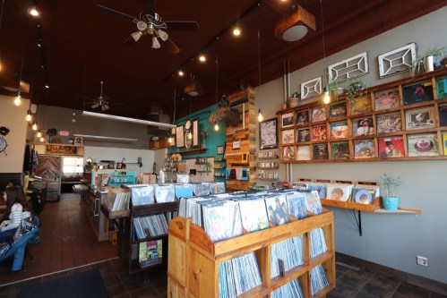 A cozy record store interior with wooden shelves, vinyl records, and colorful artwork on the walls.