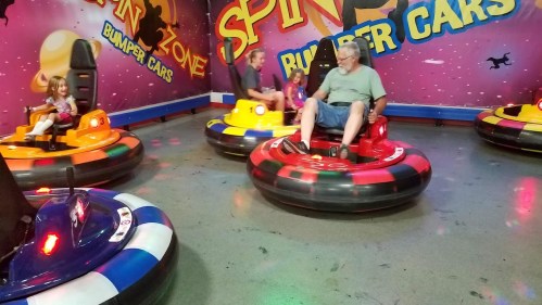 A group of people enjoying bumper cars in a colorful arcade setting, with bright lights and playful decor.