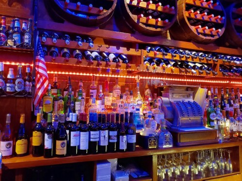 A vibrant bar display featuring various bottles of wine and spirits, with an American flag and vintage cash register.