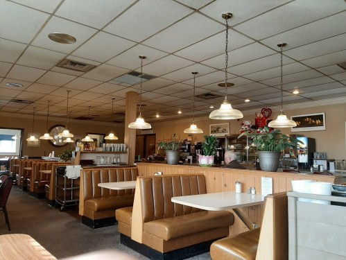 Interior of a cozy diner with wooden booths, pendant lights, and potted plants, creating a warm atmosphere.