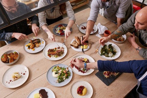 A group of people enjoying a variety of dishes at a communal table, each using forks to sample the food.