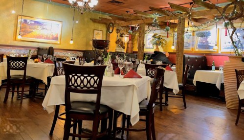 Cozy restaurant interior with wooden decor, tables set with white tablecloths, and warm lighting.