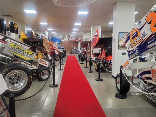 A red carpet leads through a museum displaying various colorful sprint cars and racing memorabilia.