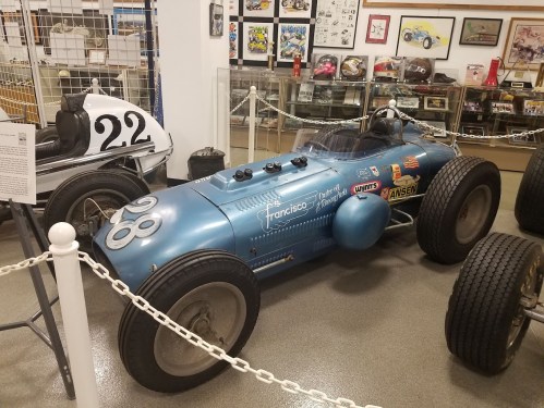 A vintage blue race car displayed in a museum, featuring a streamlined design and various sponsor logos.