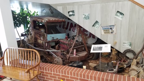 An old, rusty truck displayed in a museum setting, surrounded by vintage photos and rustic decor.