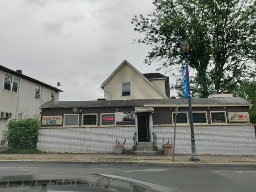 A small diner with a white brick exterior and a sign reading "Crystal Diner," surrounded by trees and cloudy skies.
