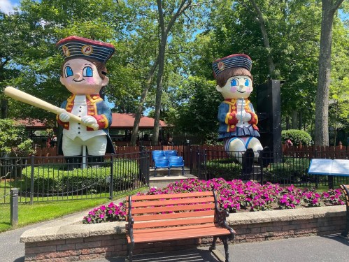 Two large cartoonish pirate statues stand in a park, surrounded by colorful flowers and a bench in the foreground.