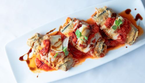 Three stuffed and breaded eggplant rolls topped with marinara sauce and garnished with herbs on a white plate.