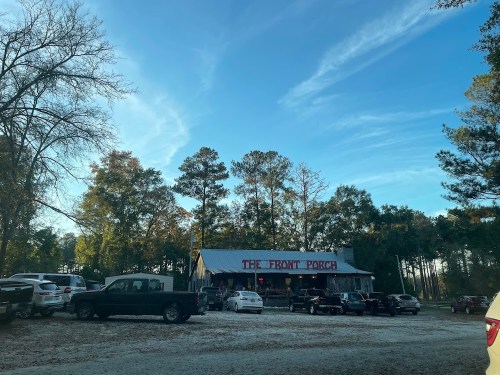 A rustic building labeled "The Front Porch" surrounded by trees and parked cars under a clear blue sky.