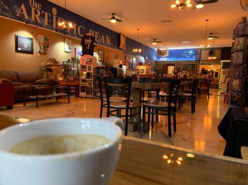 A cozy café interior with wooden tables, chairs, and a counter, featuring a cup of coffee in the foreground.