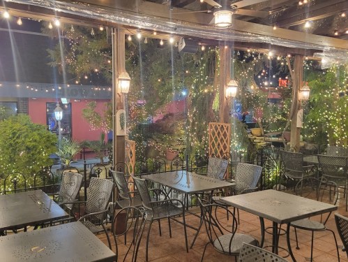 Cozy outdoor dining area with string lights, greenery, and empty tables under a covered patio.