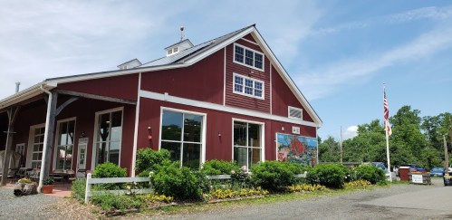 A red barn-style building with large windows, surrounded by greenery and a flag, under a clear blue sky.