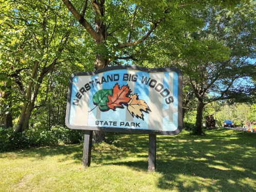 Sign for Nerstrand Big Woods State Park, featuring colorful leaves and surrounded by lush greenery.