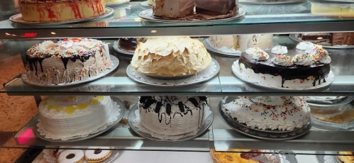 A display case filled with various decorated cakes, including chocolate, vanilla, and fruit-topped options.