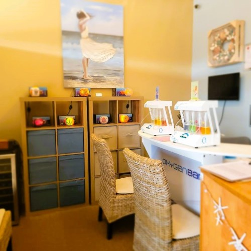 A cozy spa reception area with wicker chairs, colorful decor, and a beach-themed painting on the wall.