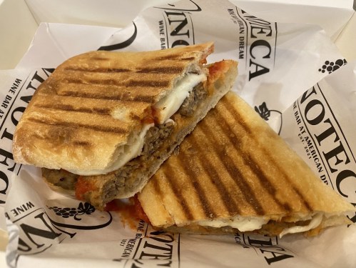 A grilled sandwich with layers of meat, cheese, and sauce, served in a branded paper wrapper.