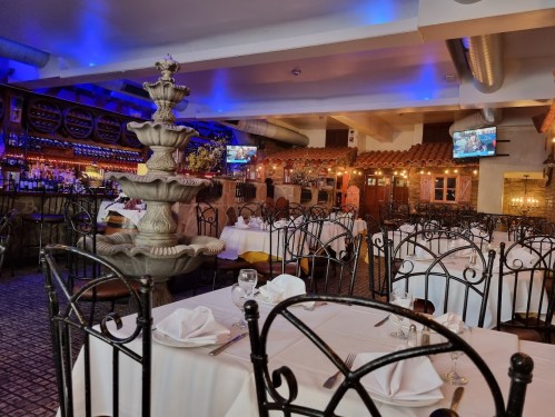 A cozy restaurant interior featuring a fountain, elegant tables, and ambient lighting with a bar in the background.