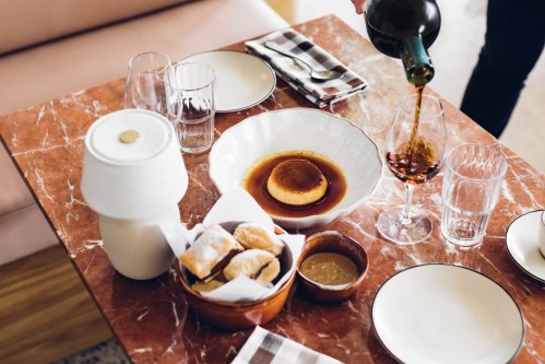 A beautifully set table with a dessert, pastries, sauces, and wine being poured into a glass.