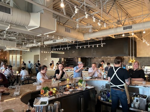 A bustling restaurant interior with patrons at tables and a bar, featuring a bartender preparing drinks.