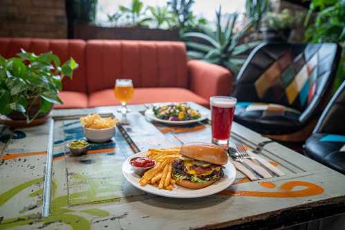 A burger with fries and condiments, a salad, and drinks on a colorful table in a cozy restaurant setting.