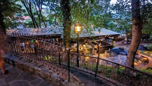 A cozy outdoor restaurant surrounded by trees, with warm lighting and tables set for dining in the evening.