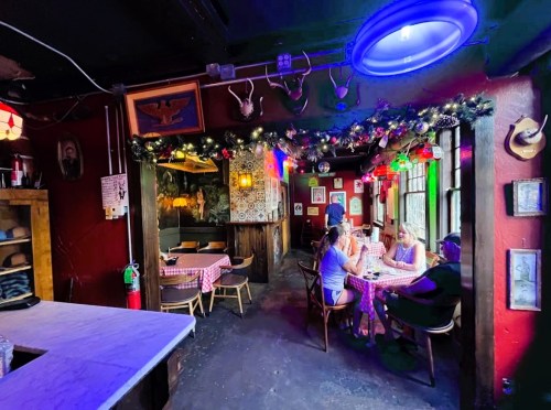 Cozy restaurant interior with colorful lights, checkered tables, and festive decorations, featuring diners at a table.