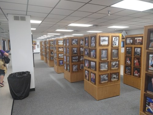 A hallway with wooden display panels filled with framed photographs, and a trash can in the corner.