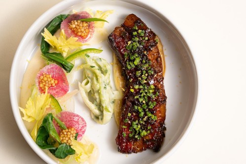 A beautifully plated dish featuring glazed meat, vibrant vegetables, and creamy sauce, garnished with herbs.