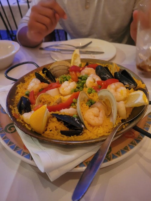A colorful seafood paella with shrimp, mussels, clams, and vegetables served in a round dish.