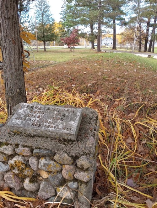 A weathered stone marker surrounded by grass and fallen leaves, with trees in the background.