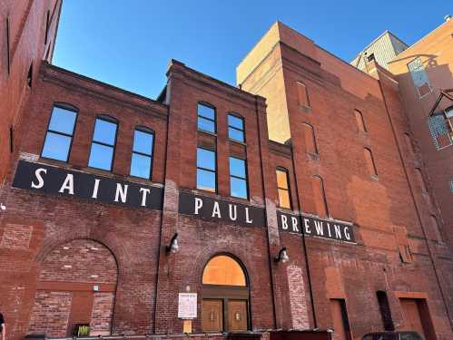 Exterior of Saint Paul Brewing, featuring red brick walls and large windows under a clear blue sky.