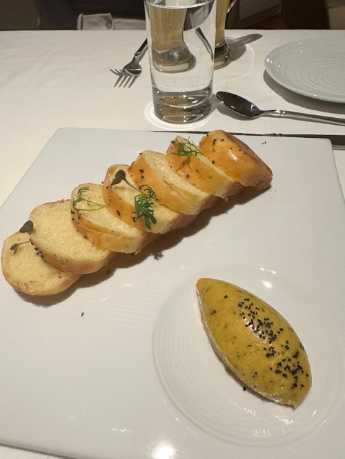 Sliced bread with herbs on a plate, accompanied by a dollop of yellow sauce with black seeds.
