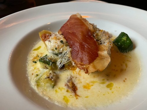 A gourmet dish featuring a crispy topping, creamy sauce, and vegetables, elegantly presented on a white plate.