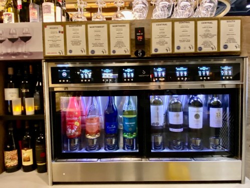 A wine dispenser with various bottles and menus displayed above, showcasing different wine options.
