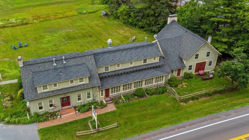 Aerial view of a large green house with a sloped roof, surrounded by grass and trees, near a road.