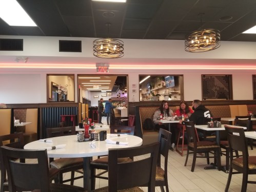 A modern restaurant interior with tables, diners, and decorative lighting, featuring a warm and inviting atmosphere.