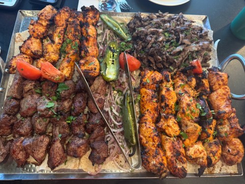 A large platter of grilled meats, including chicken and beef skewers, garnished with tomatoes, onions, and peppers.