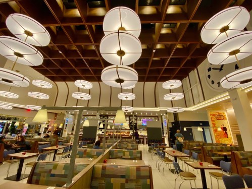 Modern restaurant interior with wooden ceiling, circular lights, and colorful seating arrangements.