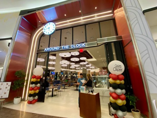 Entrance of a restaurant named "Around the Clock," featuring a clock, decorative balloons, and a grand opening sign.