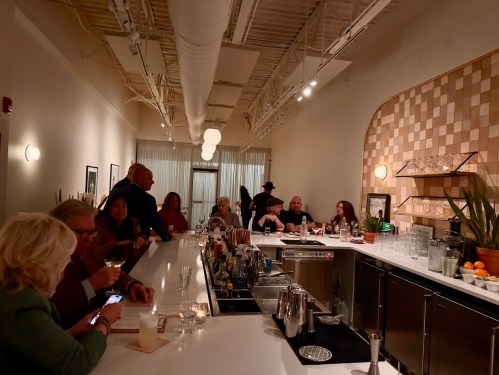 A lively bar scene with patrons socializing at a sleek counter, surrounded by plants and warm lighting.