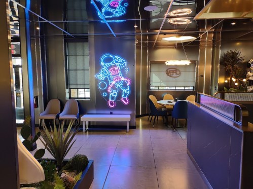 A modern restaurant interior featuring a neon astronaut mural, sleek seating, and stylish decor.