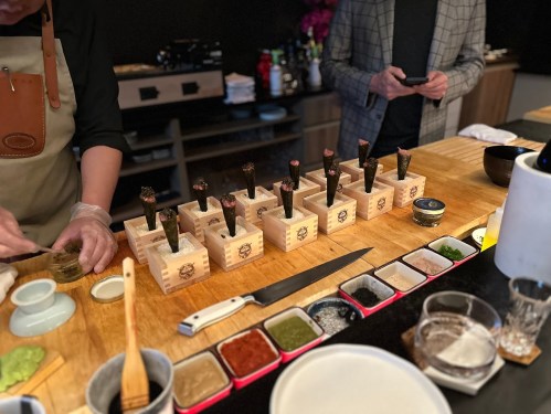 A chef prepares sushi on a wooden counter, with various sauces and ingredients arranged in front.