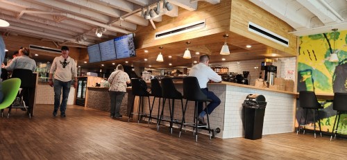 A modern café interior with a wooden bar, patrons seated, and a colorful mural on the wall.