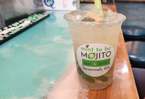 A refreshing mojito in a clear cup with ice and mint, sitting on a colorful bar counter in Savannah, GA.