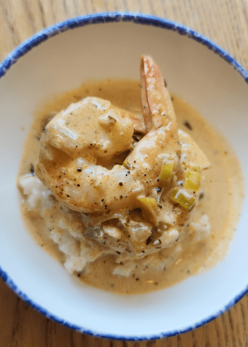 A bowl of shrimp in creamy sauce served over rice, garnished with green onions.