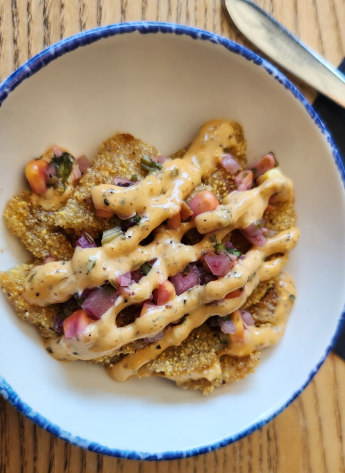 A bowl of nachos topped with salsa and a creamy sauce, served on a wooden table.